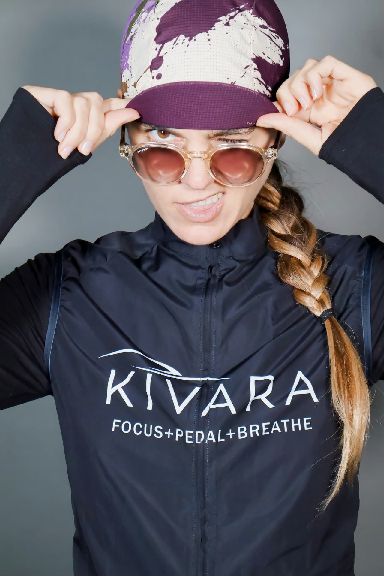 Ciclista con gorra KIVARA morada y chamarra azul marino, ajustándose la gorra