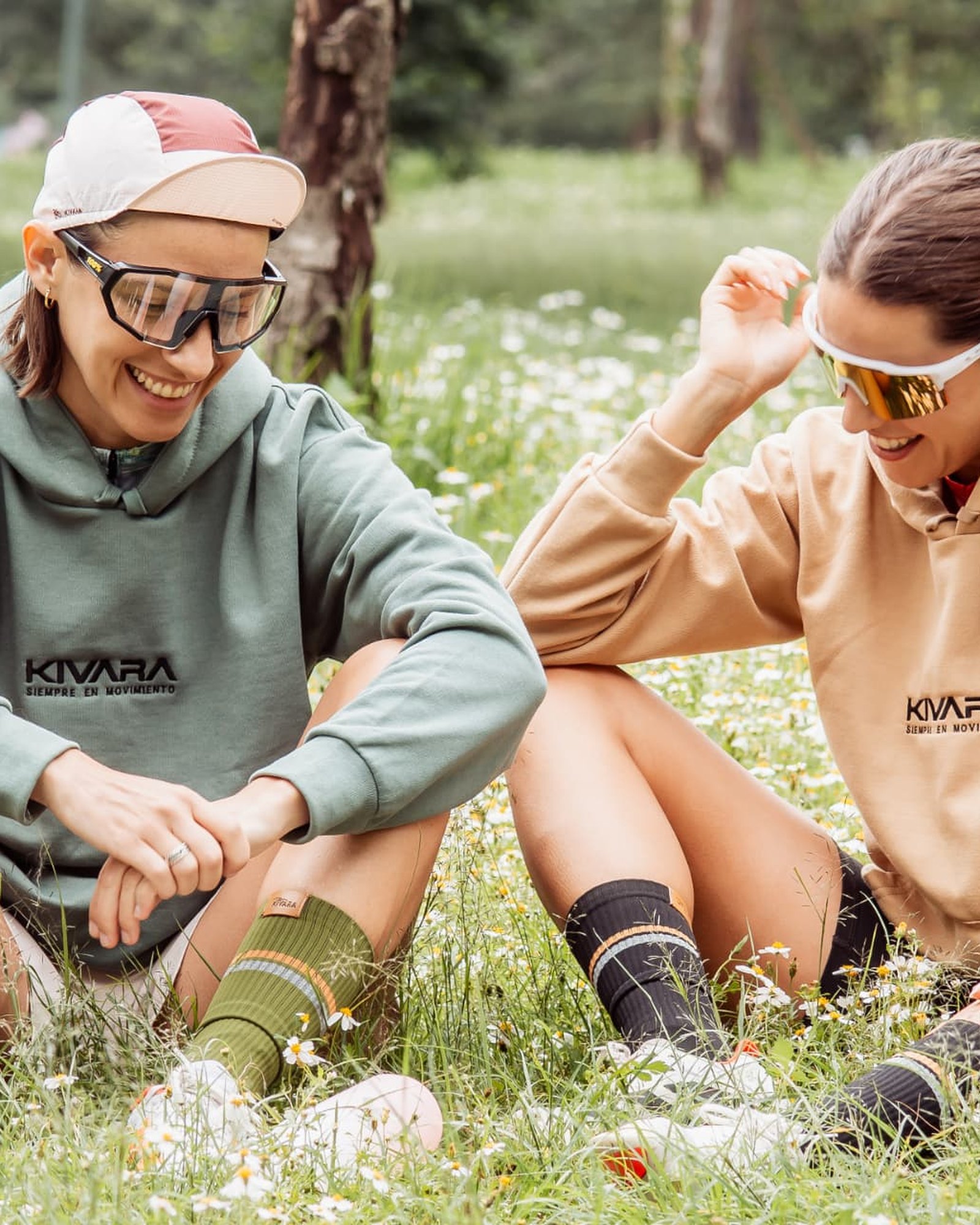 Dos ciclistas con hoodies KIVARA y calcetas de ciclismo, sentadas entre flores después de la rodada